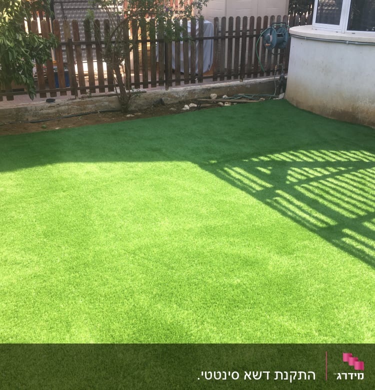 דשא סינתטי בחצר עם צינור השקיה על הקיר